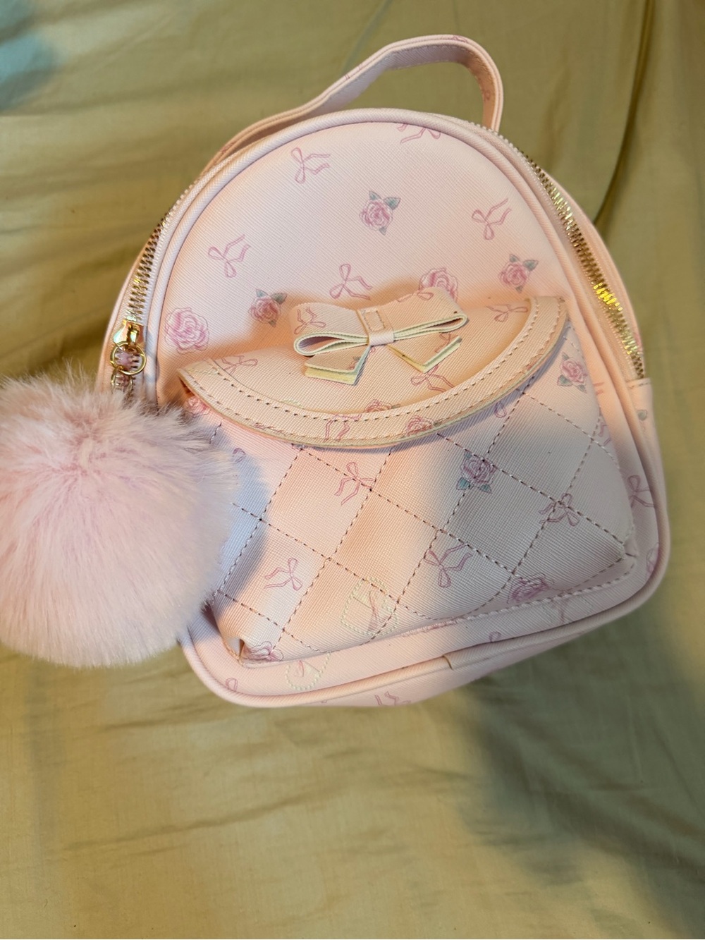 pink quilted mini backpack with a bow accent and matching pom-pom charm by Under